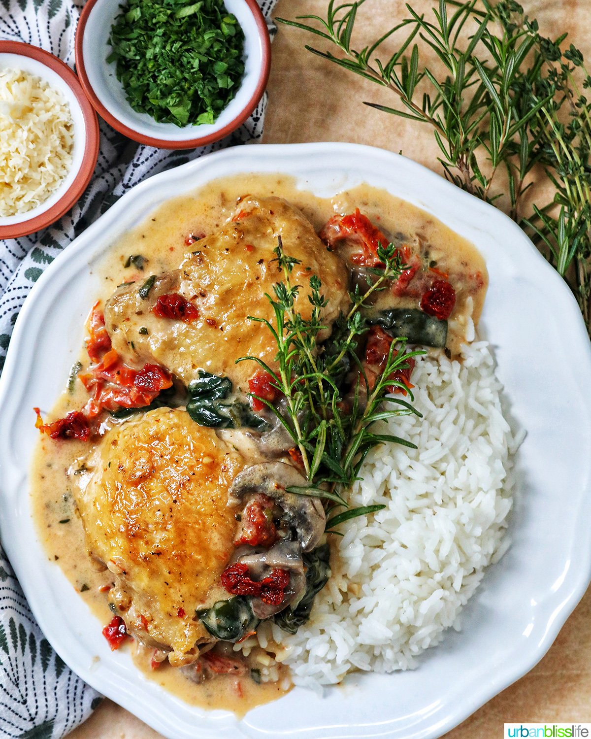 plate of dairy free marry me chicken thighs in a rich mushroom sun-dried tomato sauce with rosemary sprigs and side of rice.