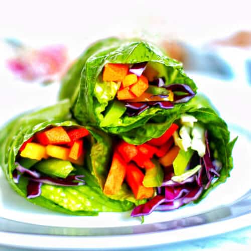three rainbow salad rolls stacked on a plate.