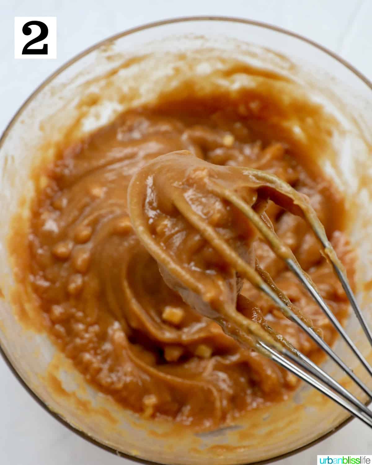 whisk in a bowl with homemade peanut sauce.