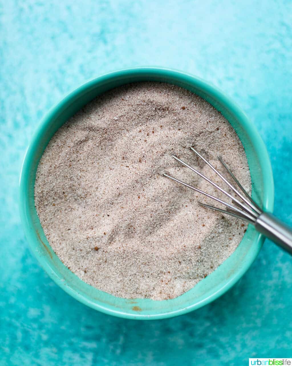blue bowl with cinnamon sugar and a whisk.