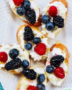 Ricotta crostini with summer berries arranged on a white serving platter.