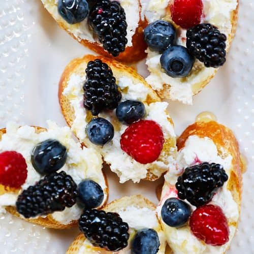 Ricotta crostini with summer berries arranged on a white serving platter.