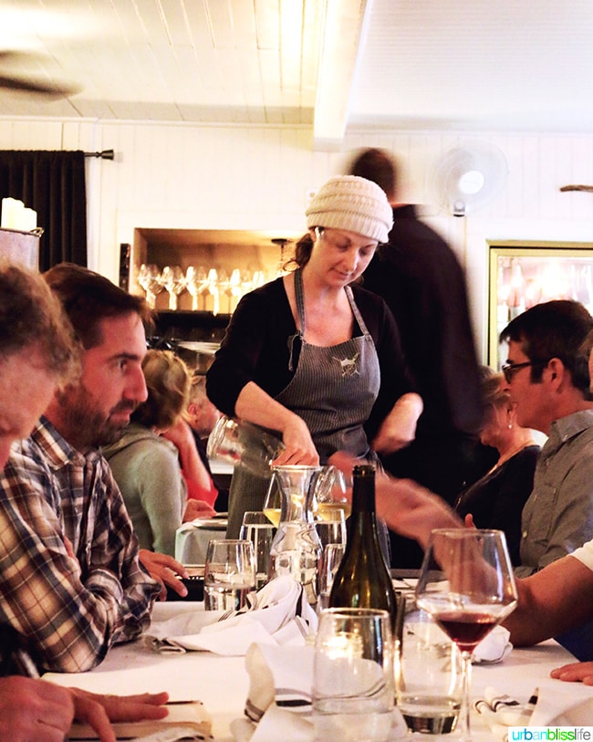 owner of The Bewildered Pig restaurant serving customers at a table.