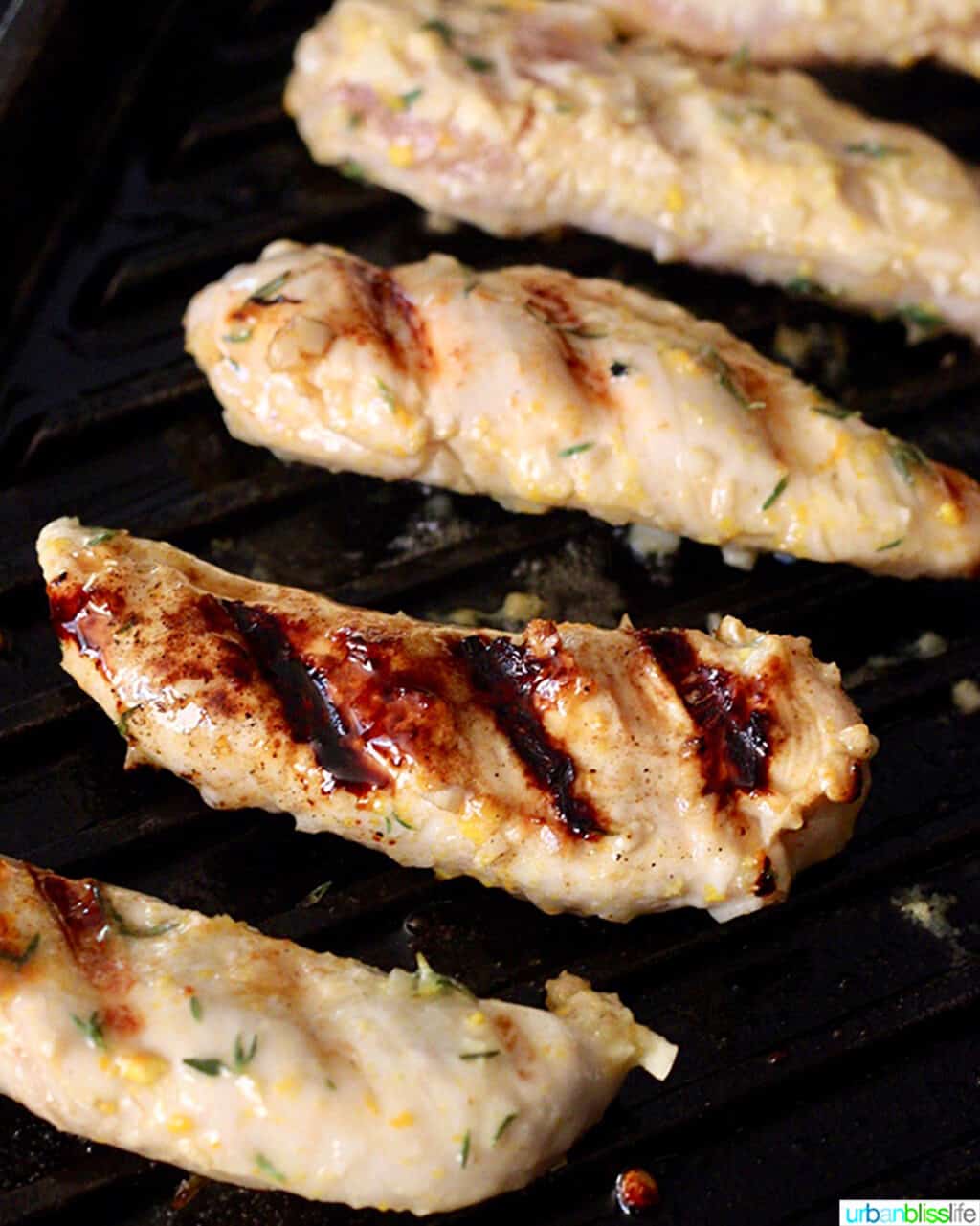 four chicken breast tenders grilling on an indoor grill pan.