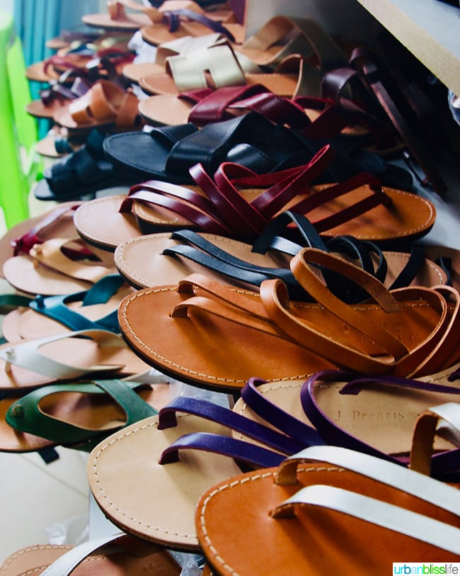 shoemaker holding up a boot and a row of sandals he made next to him in Karpathos, Greece.