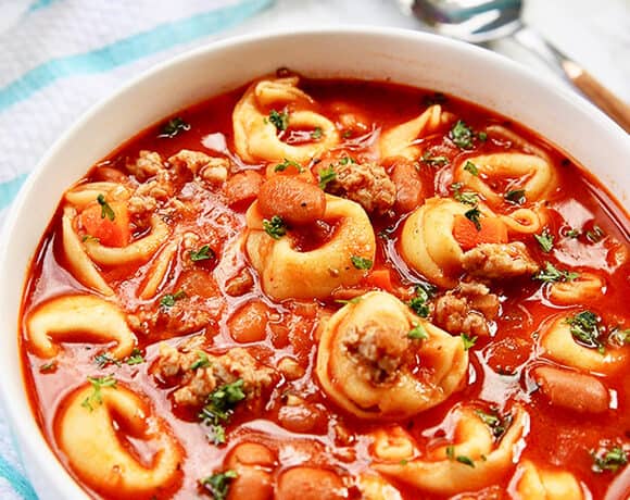 bowl of sausage tortellini soup with spoon on side