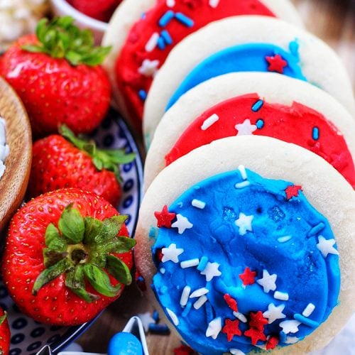 red, white, and blue frosted cookies, candies, strawberries, and blueberries plated together on a tray for 4th of July.