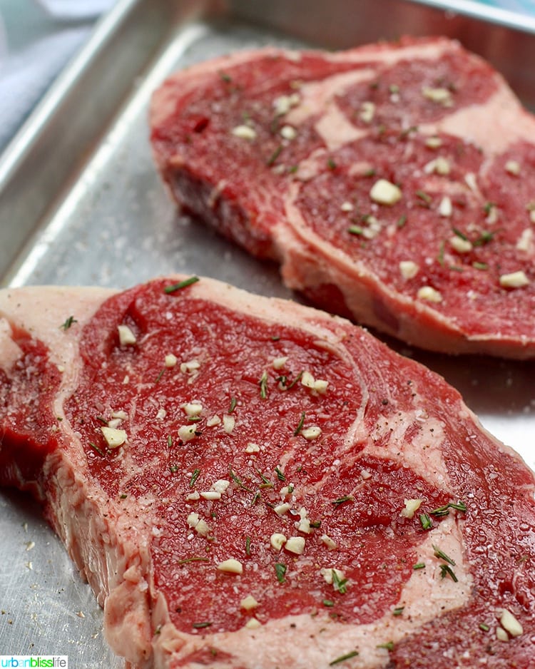 Cast iron rib eye steak raw and seasoned with salt. pepper, and garlic.