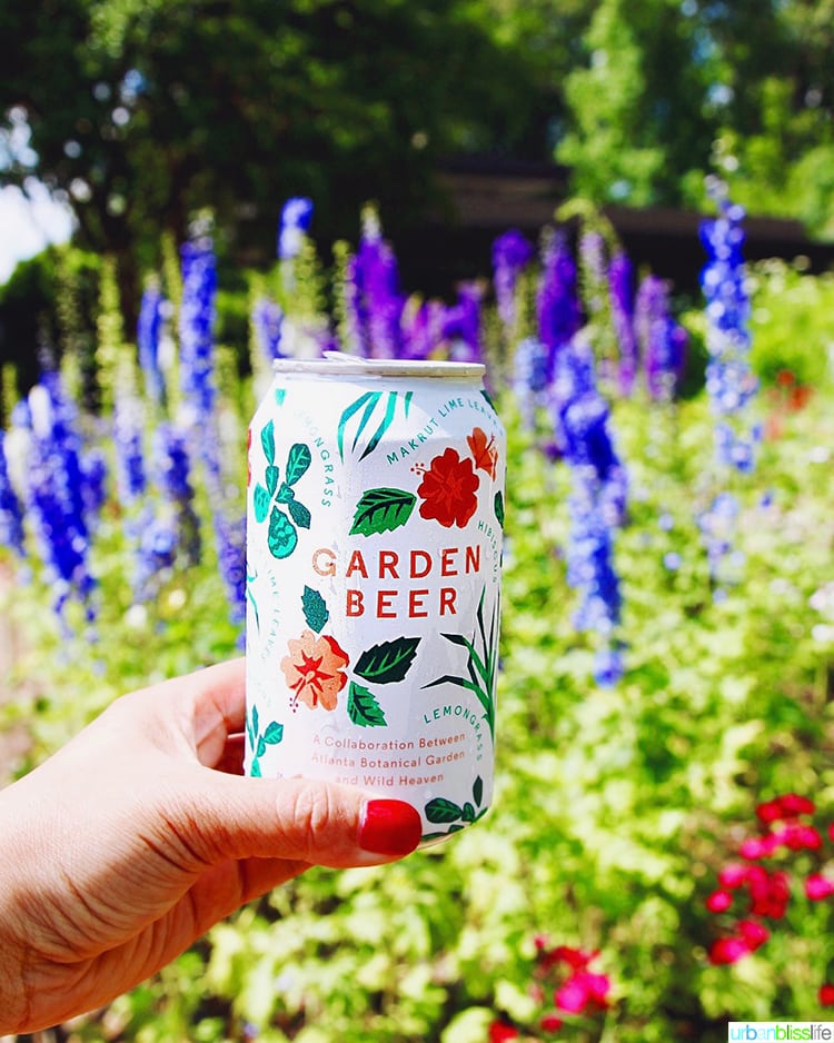 hand holding Garden Beer in front of a colorful garden.