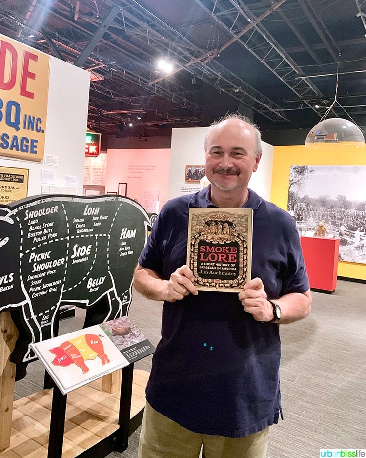 man holding a BBQ cookbook up in the middle of the museum in Atlanta.