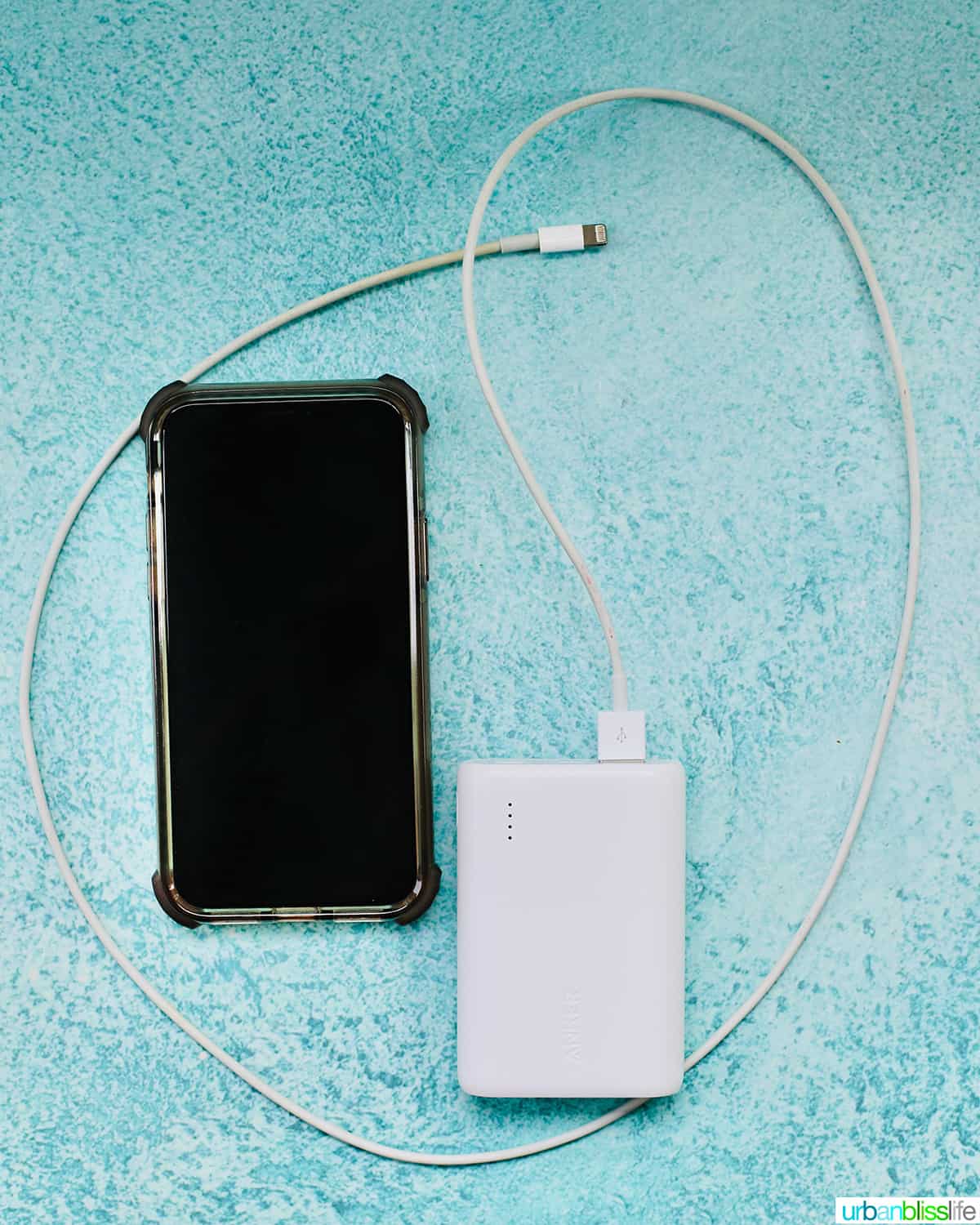 cell phone with portable charger and phone lightning cord on blue table.