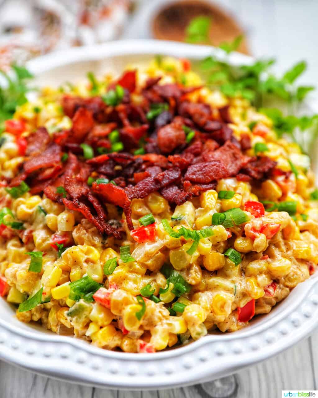 angled photo of creamy confetti corn with crispy bacon, green onions, peppers, in a white bowl.