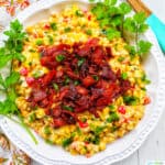 creamy confetti corn with crispy bacon, green onions, peppers, in a white bowl with greens..