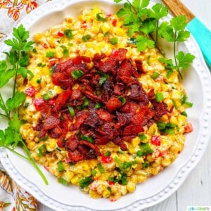 creamy confetti corn with crispy bacon, green onions, peppers, in a white bowl with greens..