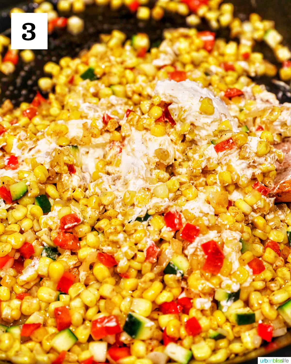 cream cheese added to corn and other veggies in a skillet.