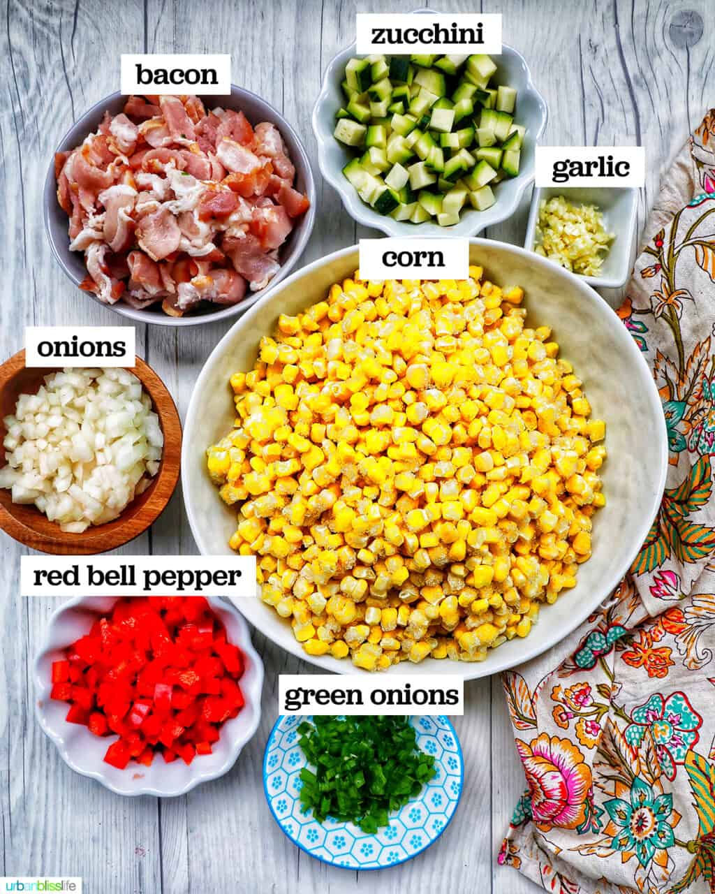 bowls of corn, peppers, zucchini, and other ingredients to make creamy confetti corn salad with a floral napkin.