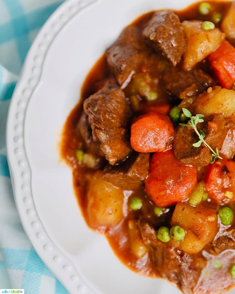 closeup half bowl of Beef stre with carrots, potatoes, and peas and fresh thyme.