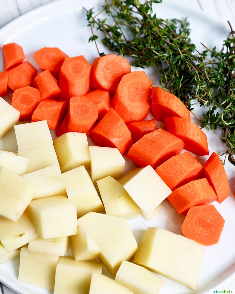 carrots, potatoes, thyme ingredients for Instant Pot Beef Stew on a white plate with a side of fresh thyme.