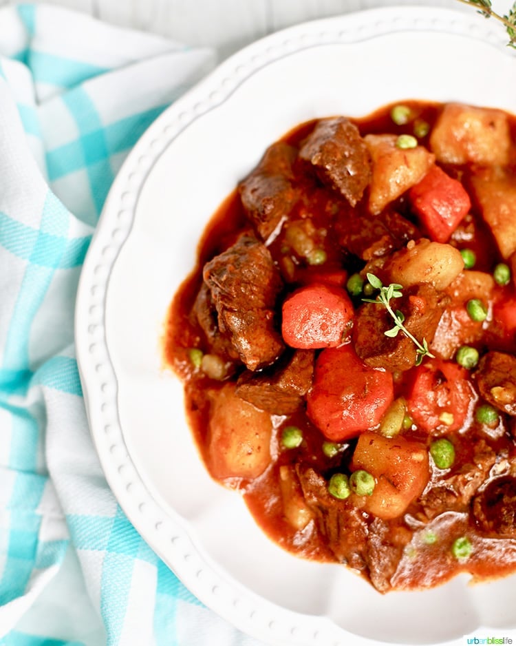 Beef stre with carrots, potatoes, and peas and fresh thyme in a large white bowl with a white and aqua napkin.