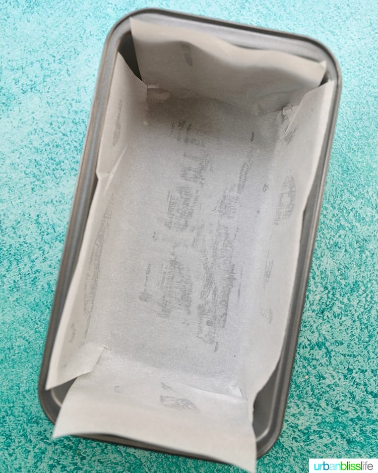 prepared loaf pan lined with parchment paper on a blue background.