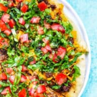 homemade taco pizza on a white plate and blue background.
