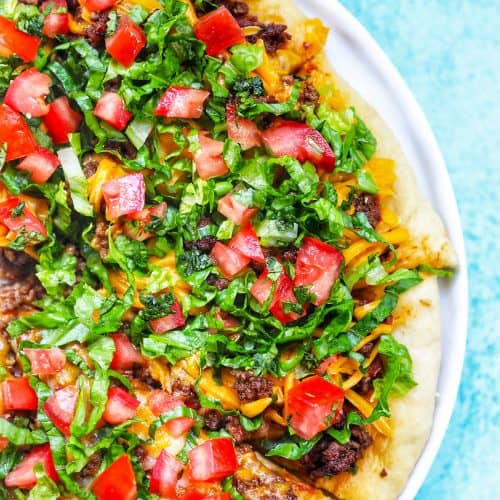 homemade taco pizza on a white plate and blue background.