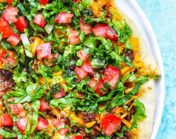 homemade taco pizza on a white plate and blue background.