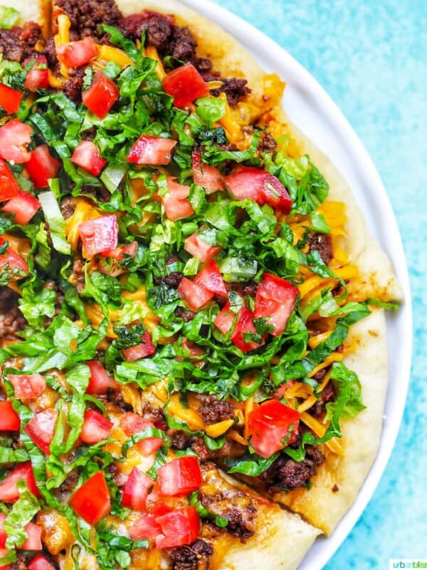 homemade taco pizza on a white plate and blue background.