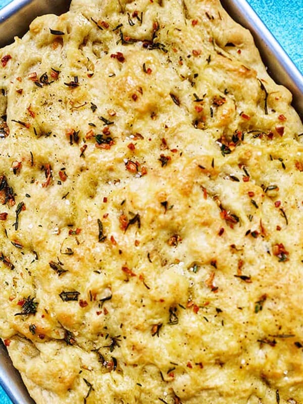 garlic rosemary focaccia bread in a baking sheet on bright blue background.