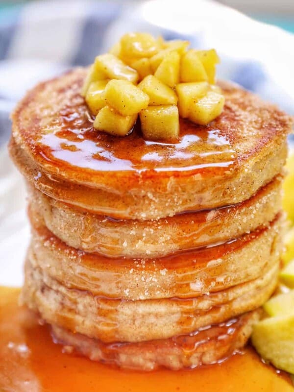 Stack of apple cinnamon pancakes topped with maple syrup and diced apples.