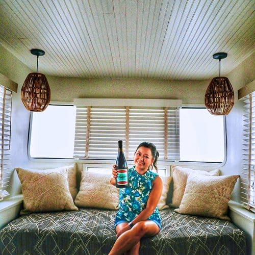 Marlynn Schotland holding up a bottle of wine inside the mansion airstream at Vintages Trailer Resort