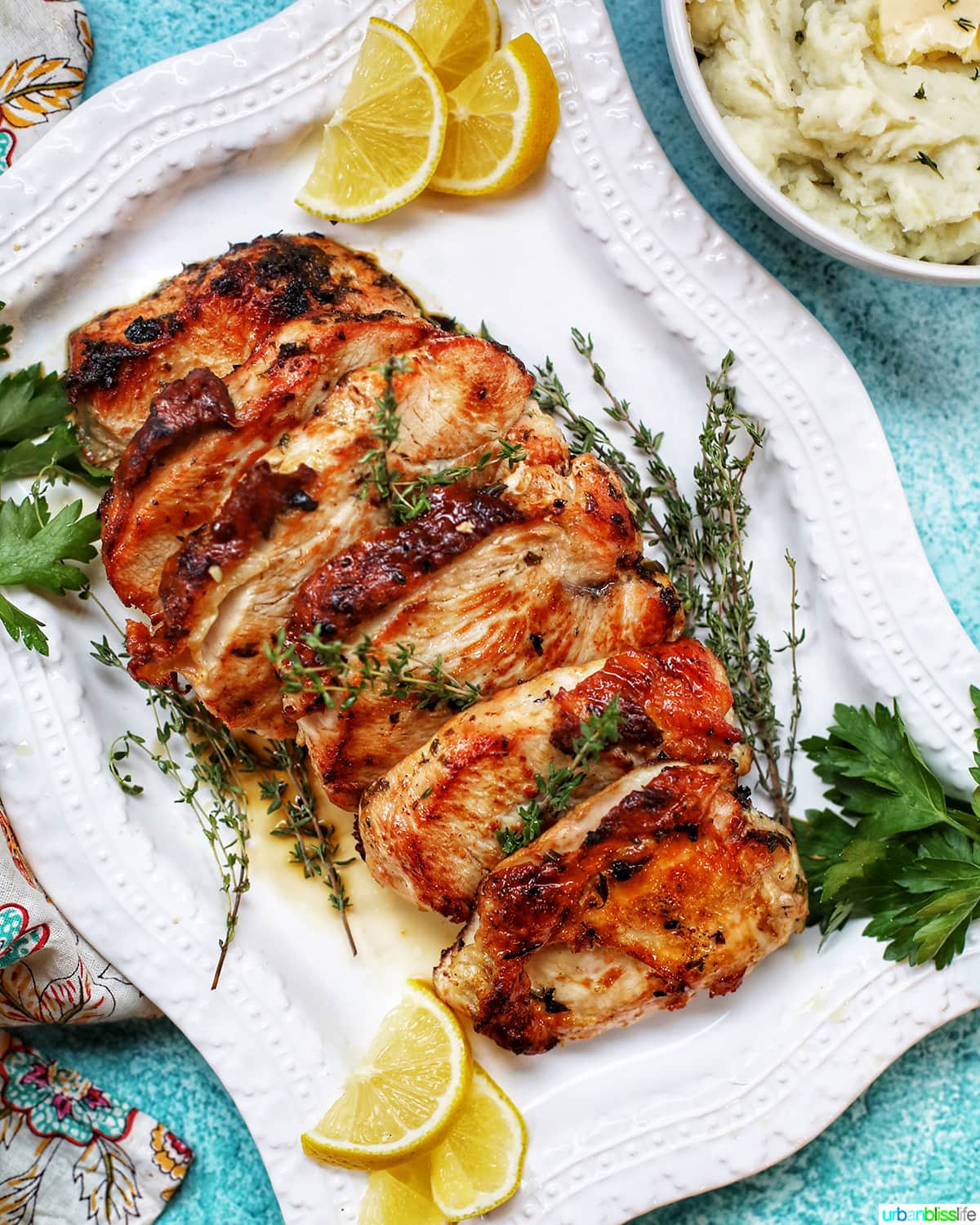 sliced Citrus Herb Turkey Breast with herbs and lemon slices on platter with mashed potatoes.