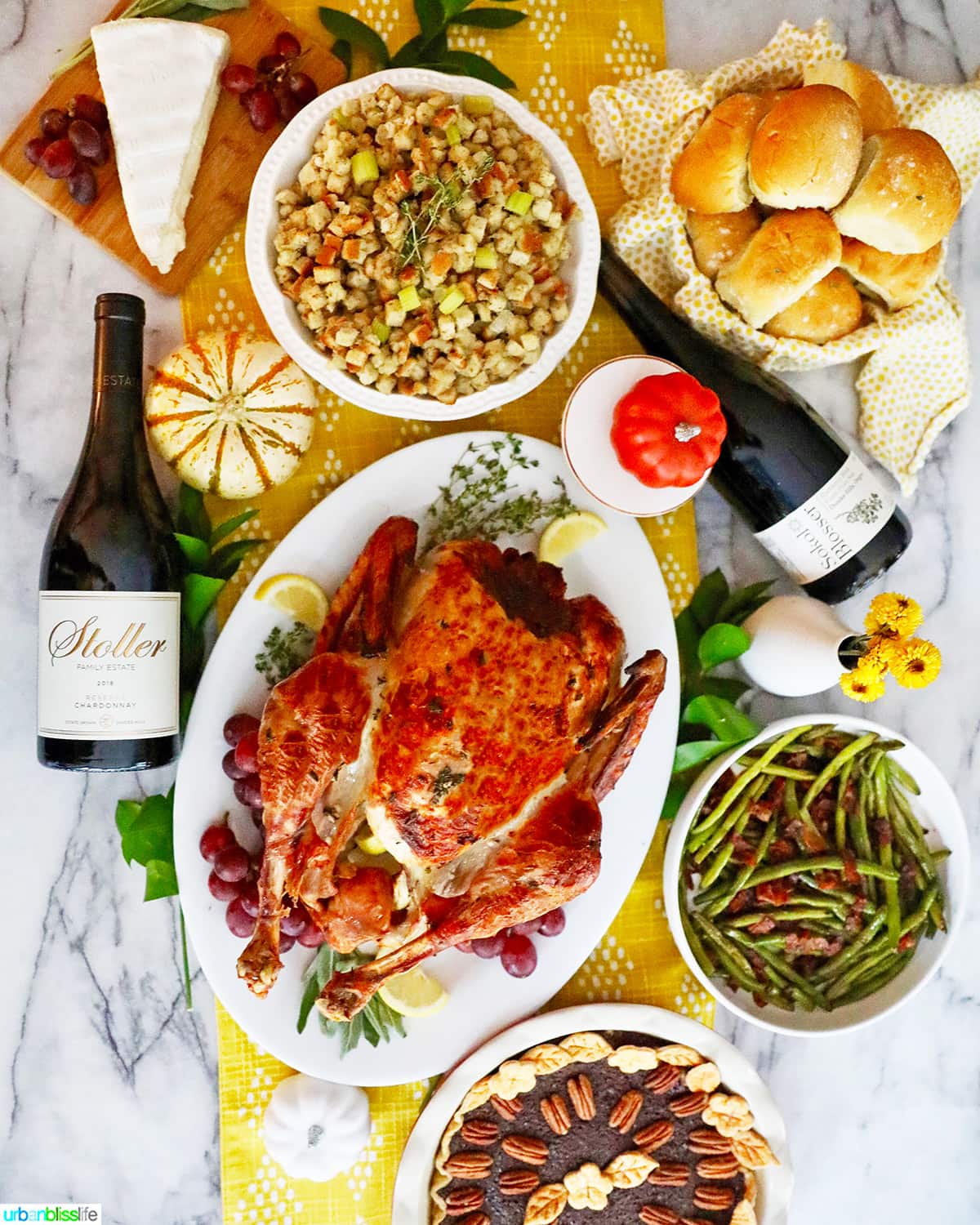 Thanksgiving dinner table with turkey, stuffing, wine, green beans, rolls and cheese.