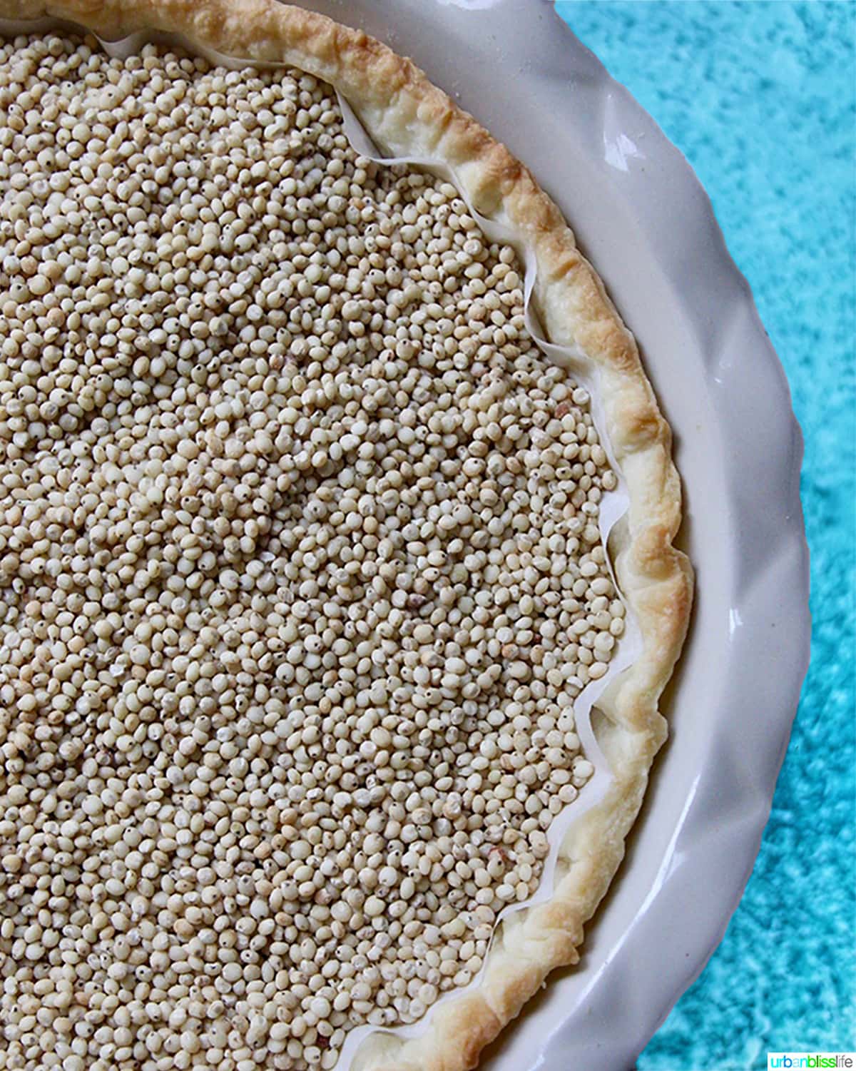 pie crust with pie weights in a pie pan on blue table.