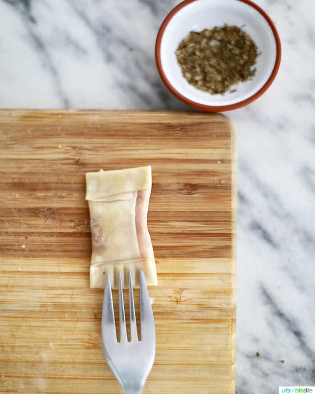 a fork securing edges of air fryer pizza rolls on a cutting board