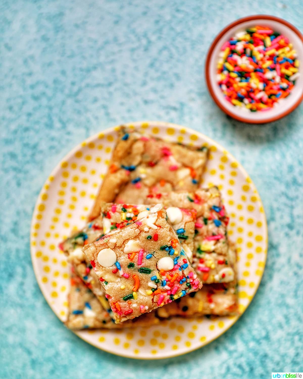 Funfetti Bars on a yellow plate with bowl of sprinkles