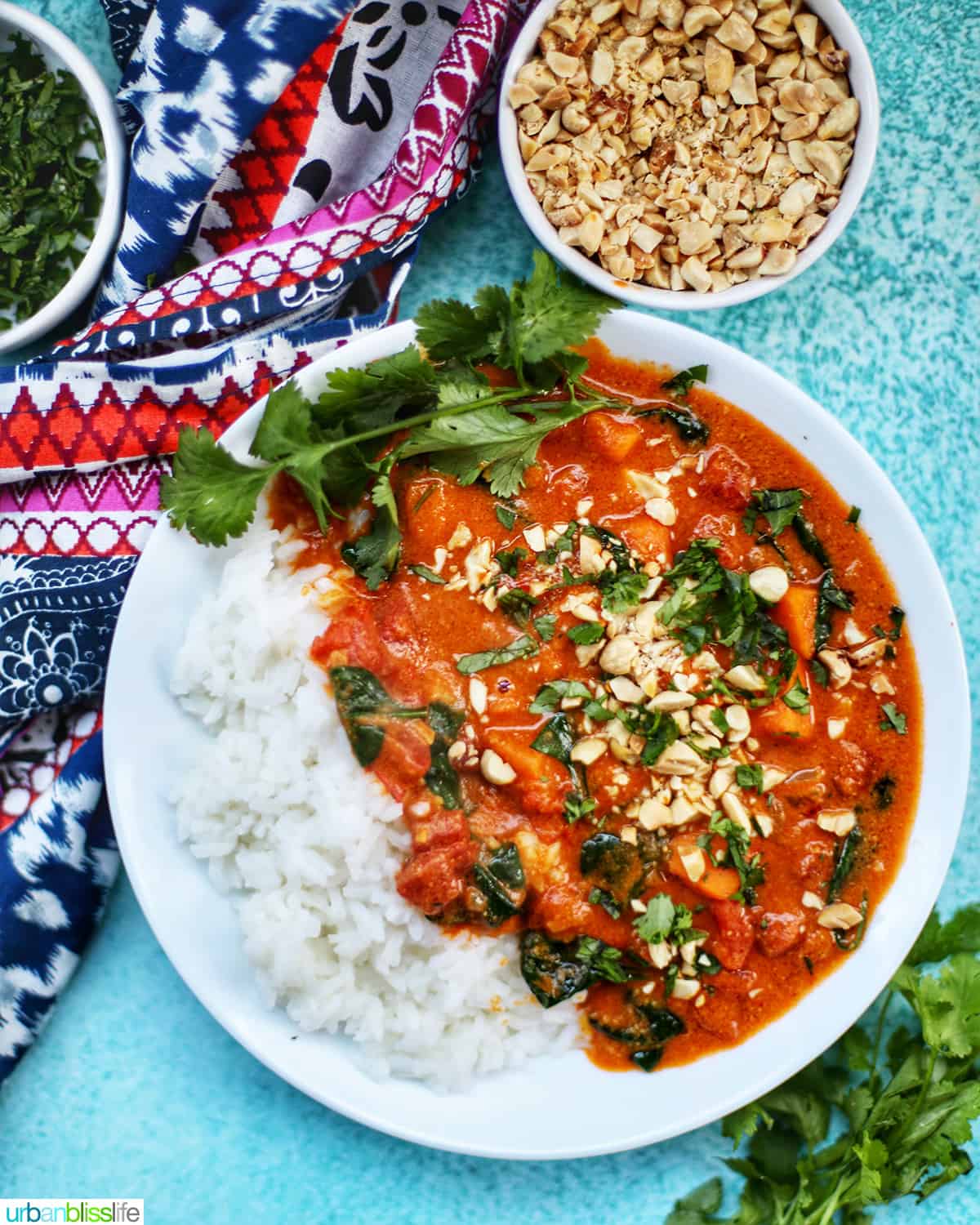 Instant Pot African Peanut Stew topped with chopped peanuts and parsley, on a bed of rice with a side of peanuts on a blue table.