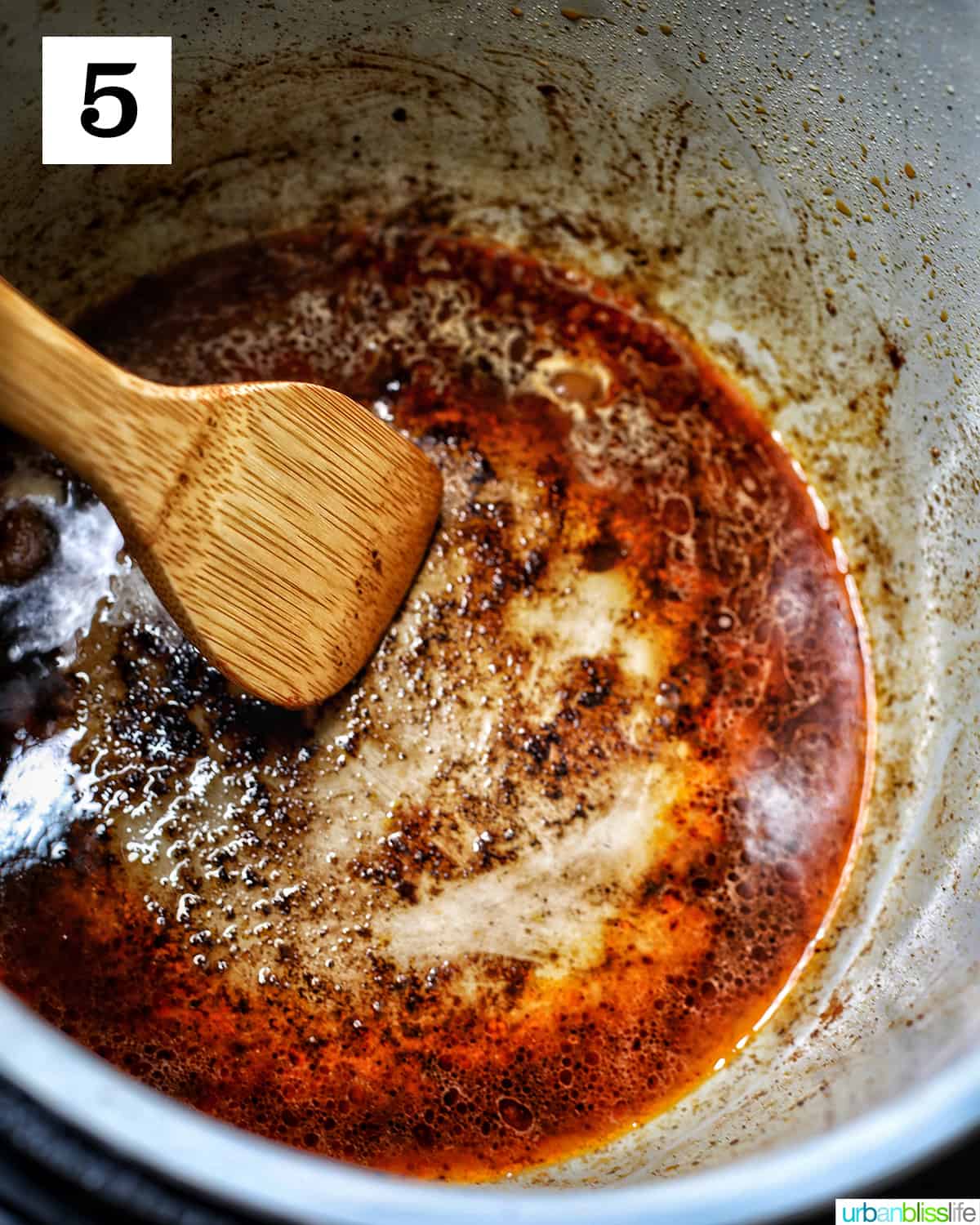 wooden spoon scraping up brown bits deglazing an instant pot with broth.