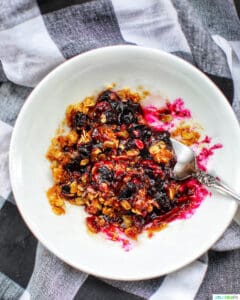 microwave blueberry crisp in a white bowl with checkered backgroud