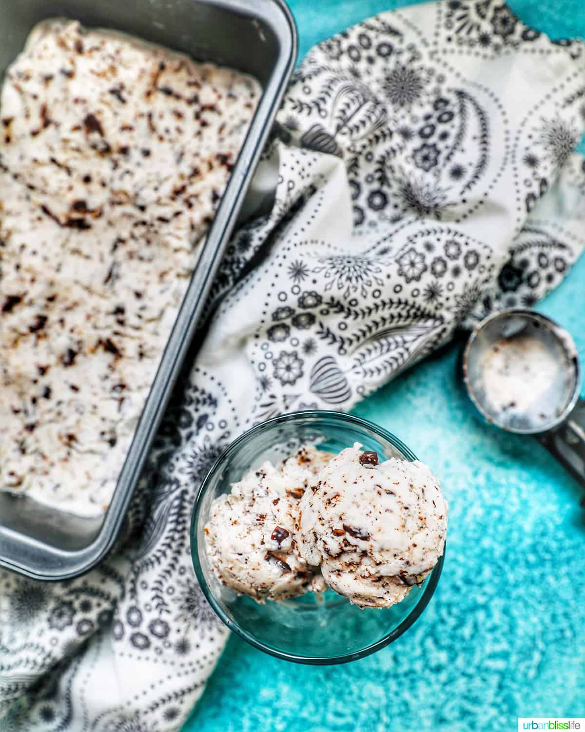dairy-free chocolate chip ice cream in an ice cream scoop next to a pan of ice cream on a blue background.