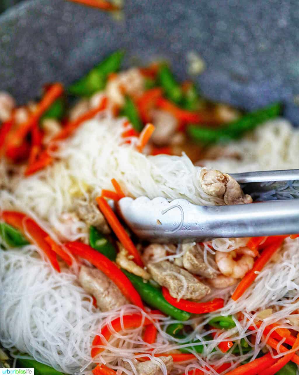 tongs mixing noodles into Filipino Pancit Bihon