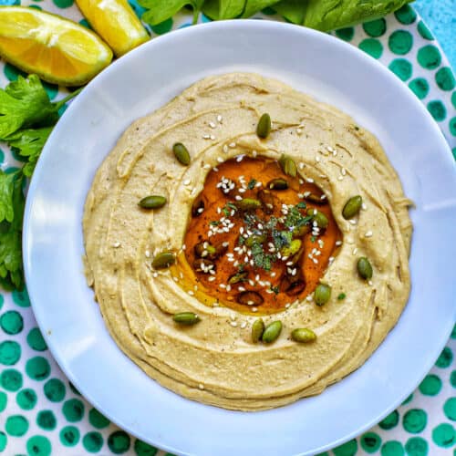 hummus in a white bowl on green polka dot platter with lemon slices