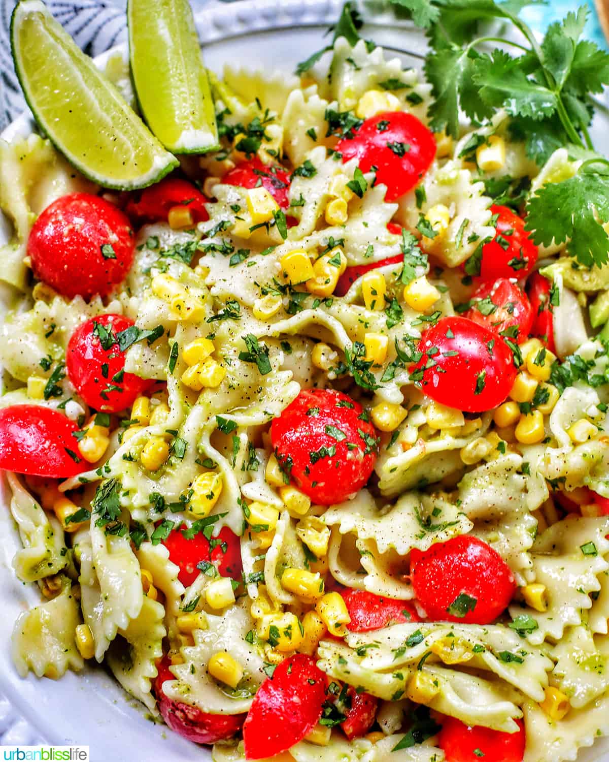 avocado salad with tomatoes and corn in a big white bowl with lime wedges.