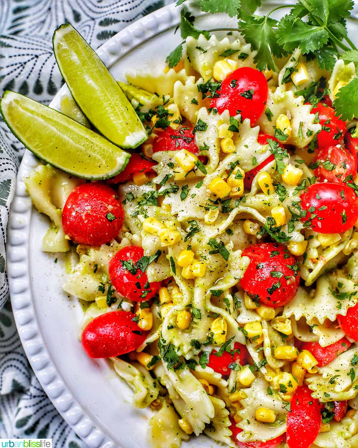 avocado salad with tomatoes and corn in a big white bowl with lime wedges.