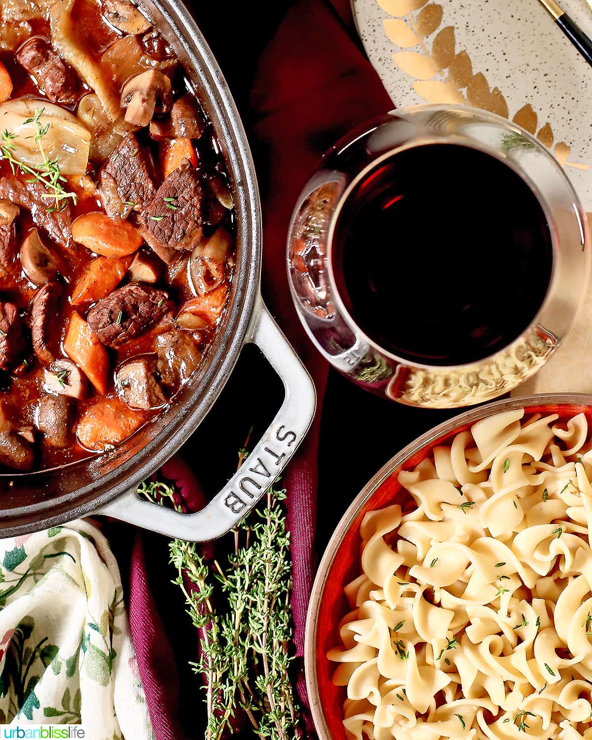 dutch oven with beef bourguignon, glass of red wine, and side of pasta.
