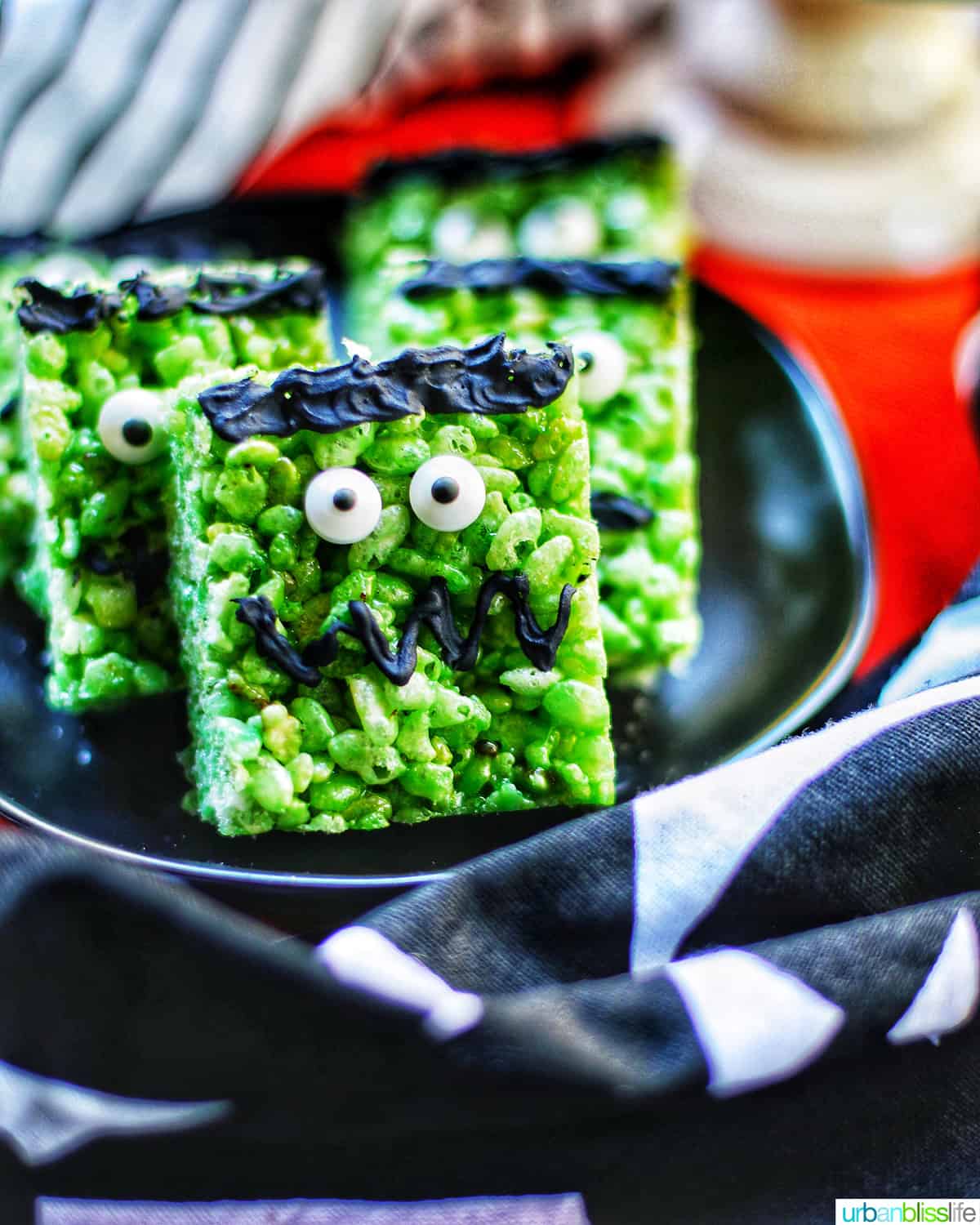 Close up of Frankenstein Rice Krispie Treats on top of black plates and orange background.