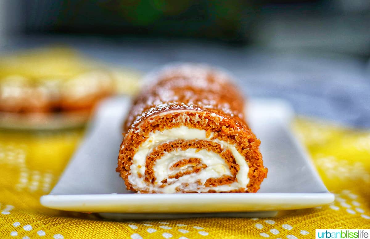 pumpkin cream cheese roll up on a white plate and yellow tablecloth.