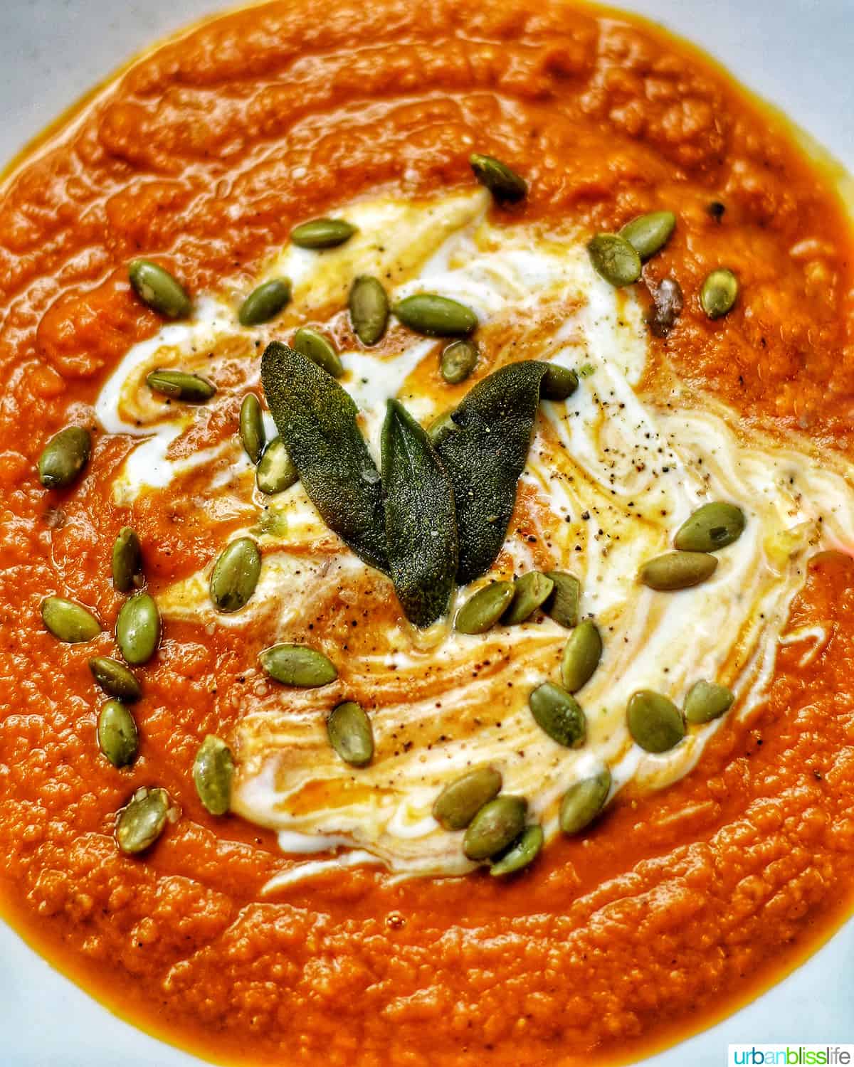 bright orange vegan pumpkin soup closeup topped with crispy sage leaves, pumpkin seeds, and dairy-free sour cream.
