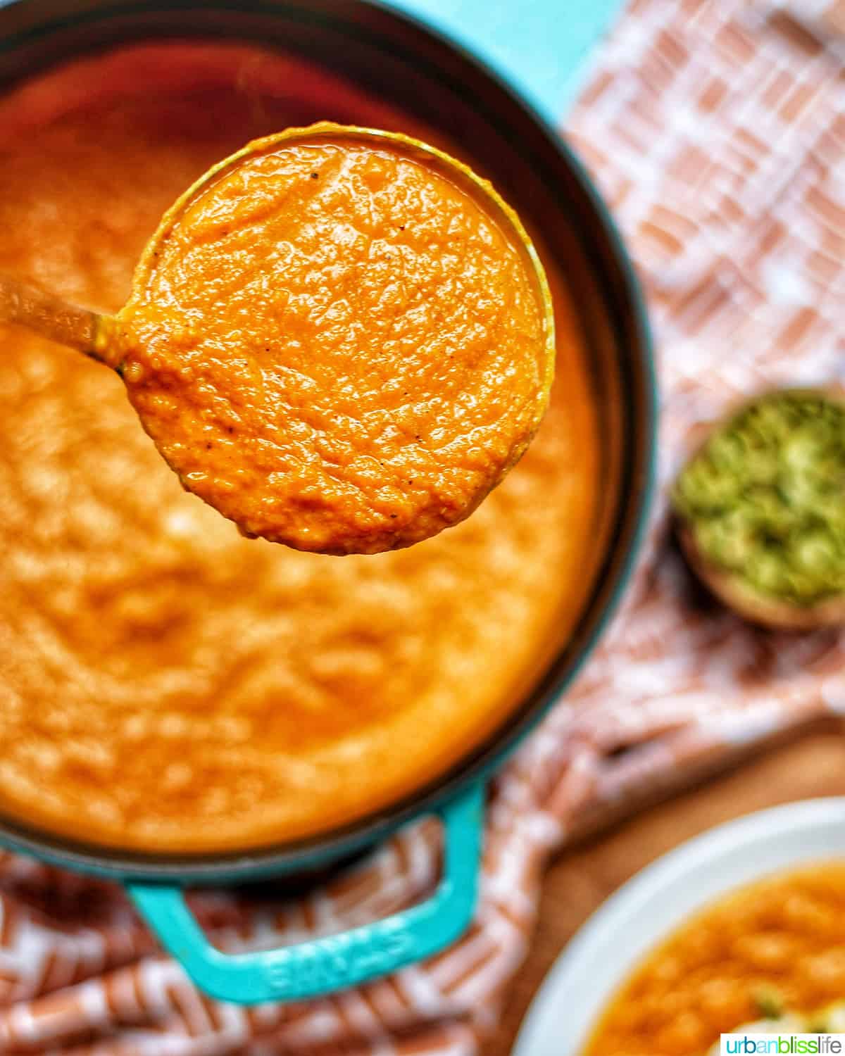 pumpkin soup without cream in ladle with dutch oven filled with pumpkin soup in background and pumpkin seeds.