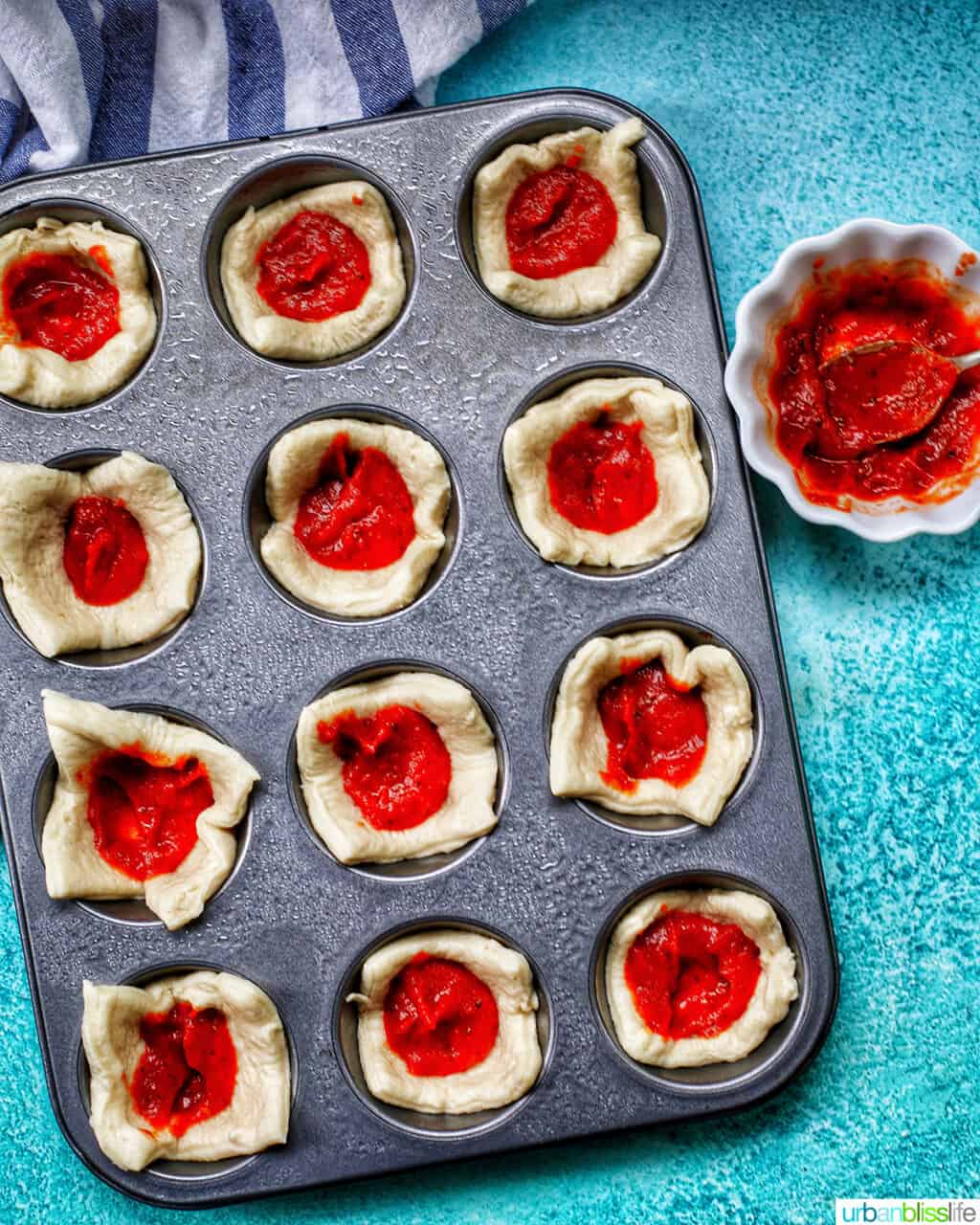 adding pizza sauce to pizza crust in muffin tins